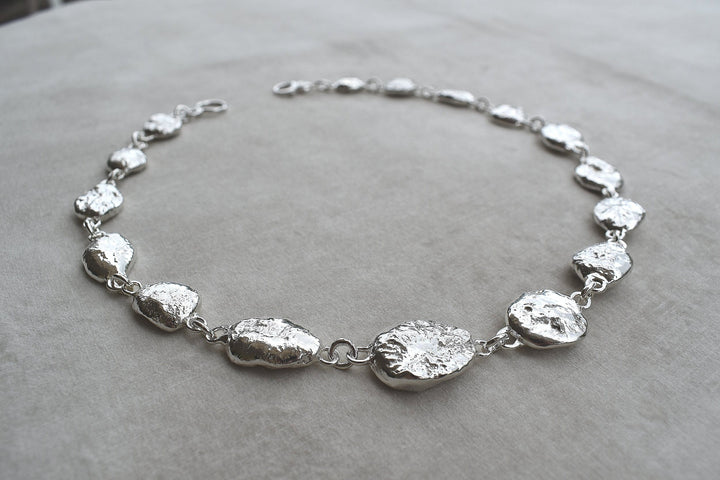 Silver pebble charms all linked together with a large handmade toggle clasp. This is a real heavy statement piece that is made to order and totally unique.
Unique silver pebble links make up this heavy statement necklace. Made to order from recycled silver each pebble is totally unique. Hallmarked for silver. silver nugget chain necklace silver charms linked together. heavy silver pebble pendant
Chunky silver nugget heavy silver chain necklace. Heavy link hermes chain choker.