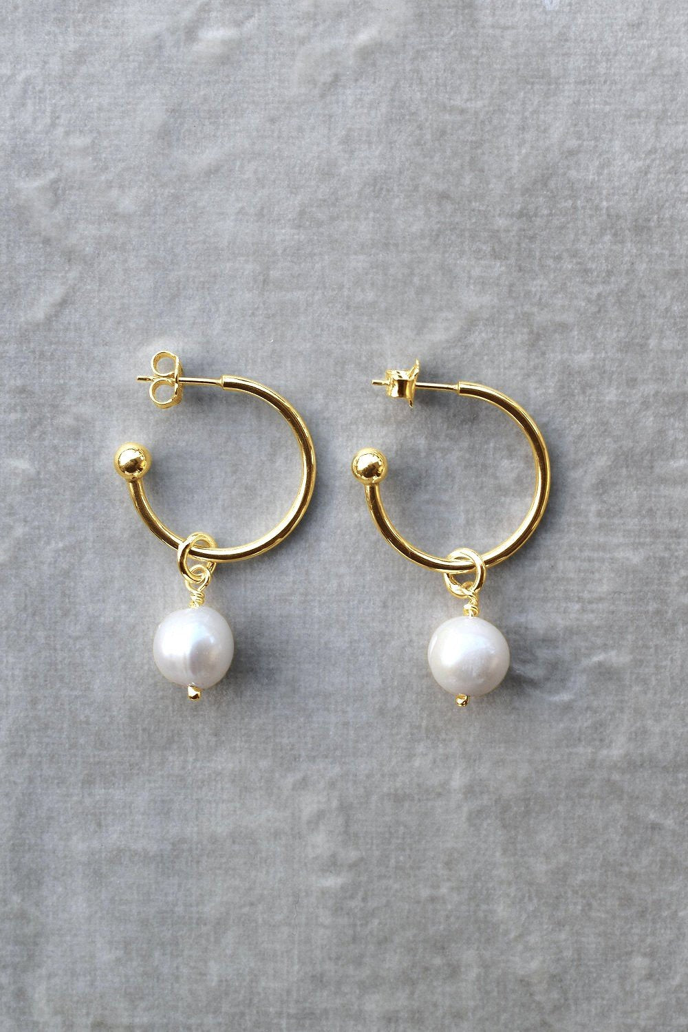 Large hoop earrings in 9ct yellow gold with white freshwater pearl drops, displayed on a textured grey background. gold hoop earrings pearl earrings hoops with charm